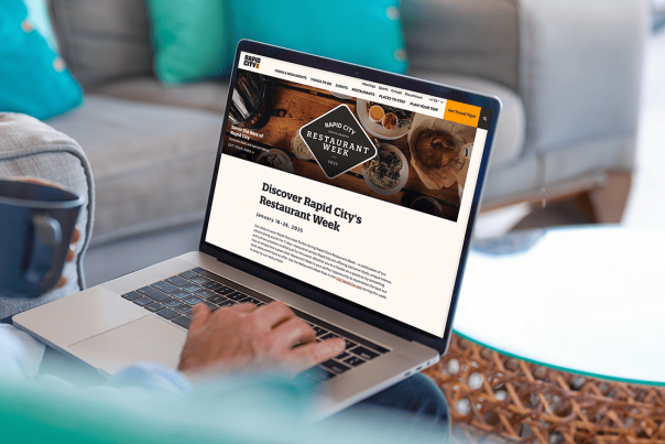 A person holding a coffee mug while browsing the Visit Rapid City website on their Macbook.